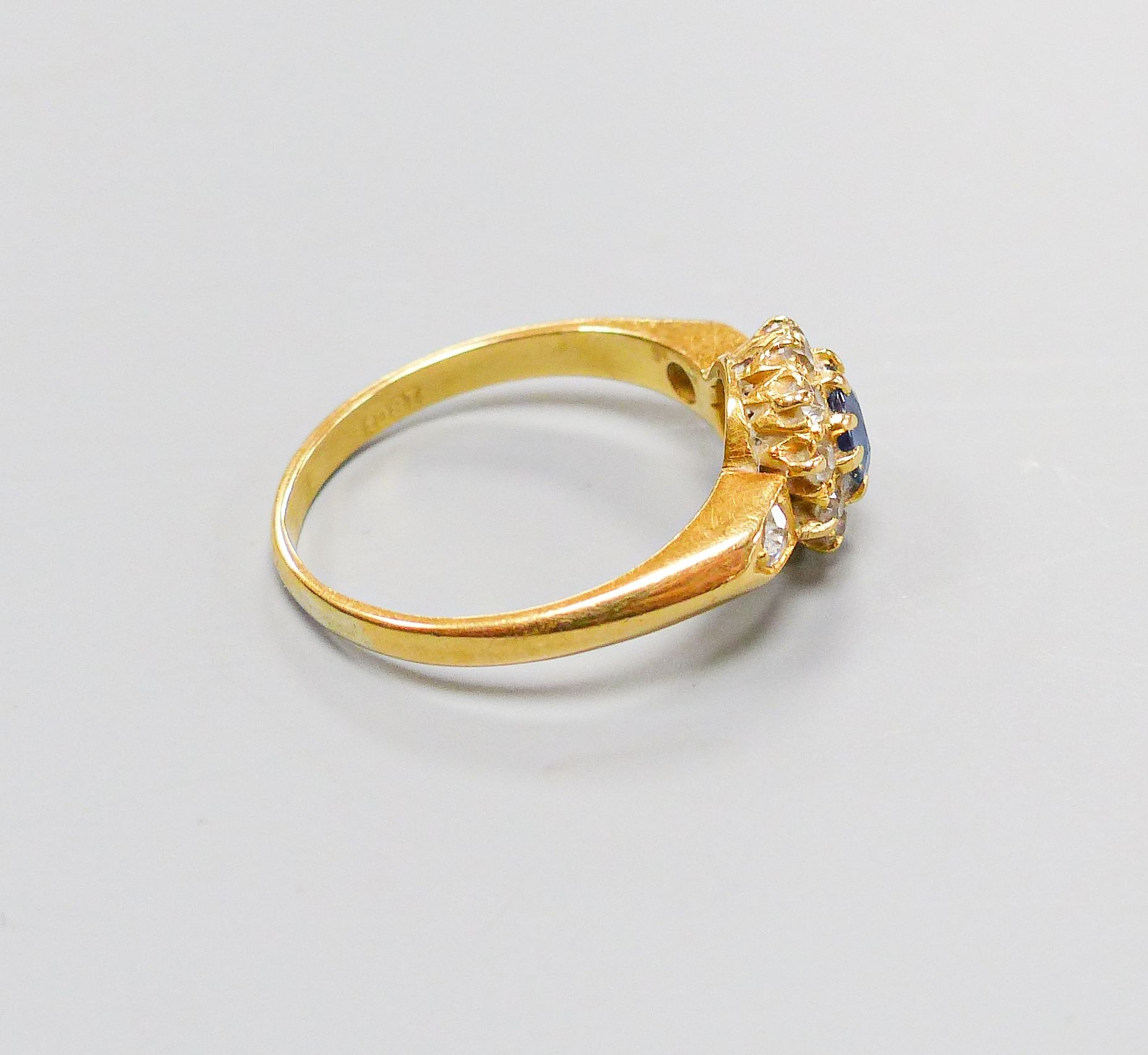 An 18ct, sapphire and diamond set circular cluster ring, with diamond set shoulders, size M, gross 3.4 grams.